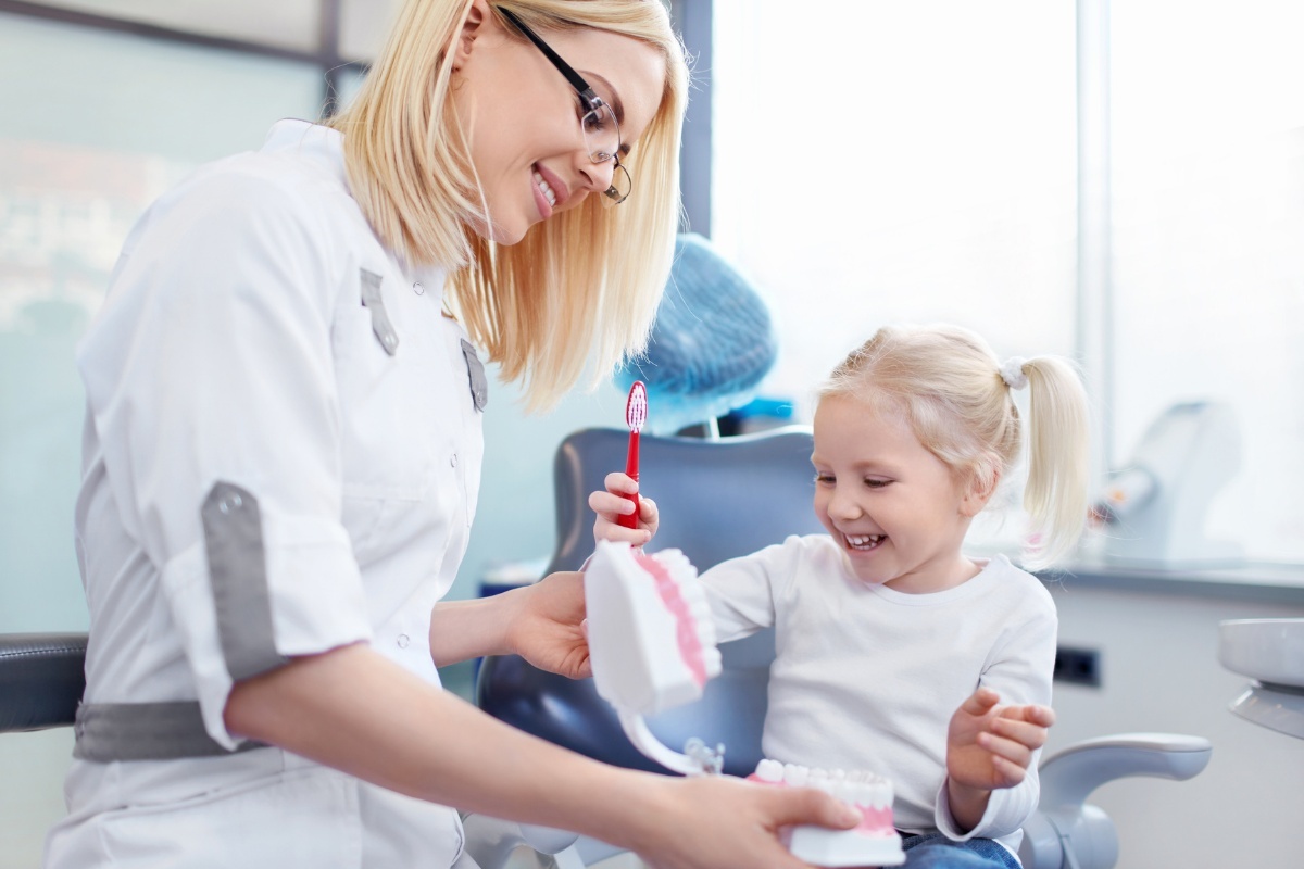 Pediatric dentist teaching young child proper toothbrushing technique in dental office.