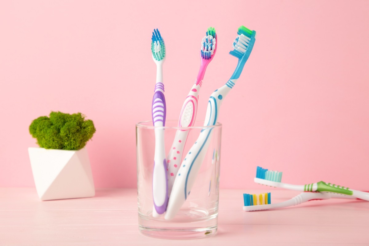 What to Do With Your Toothbrush After Being Sick Colorful toothbrushes in a clear glass with moss plant on pink background.