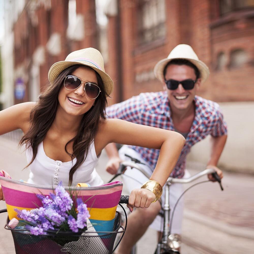 Couple Wearing Sun Hats and Sunglasses Taking a Cycle in Town on Two Bikes after Visiting One Eleven Dental Care