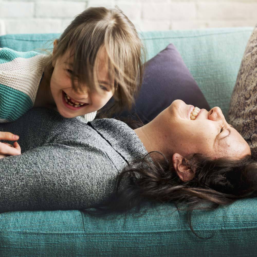 Photo of Mother and Child Laughing on the Couch and Playing after visiting One Eleven Dental Care