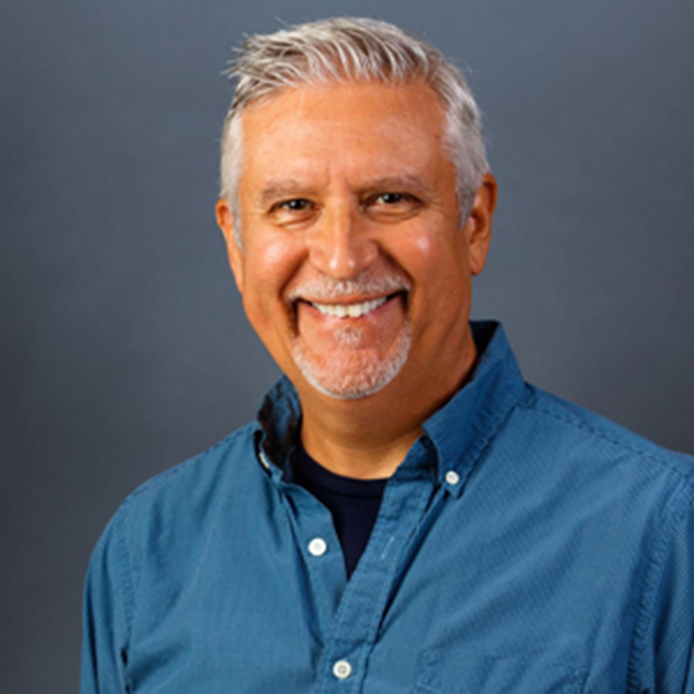Portrait of Smiling Senior Man Wearing a Dark Blue Shit with a Blue Background after Visiting One Eleven Dental Care