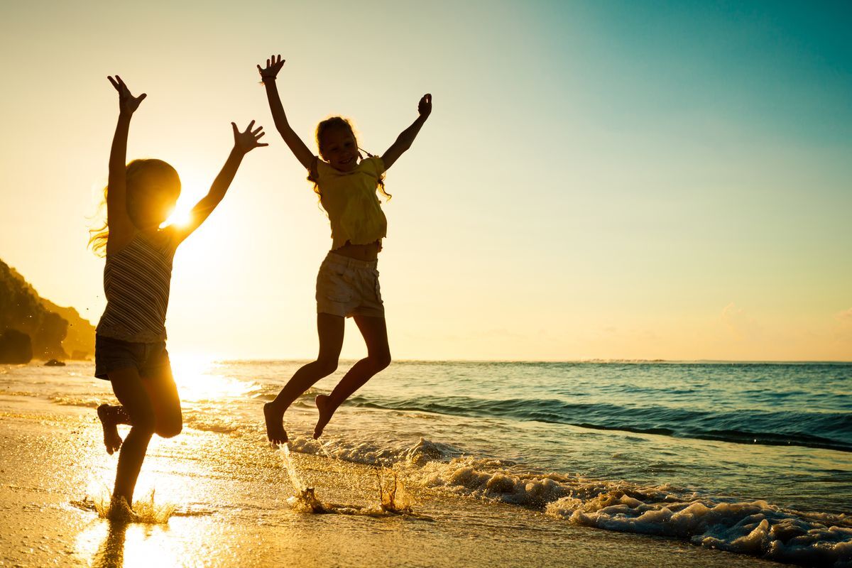 Summer Hydration Two children jumping joyfully in ocean waves at sunset, celebrating summer hydration and dental wellness.