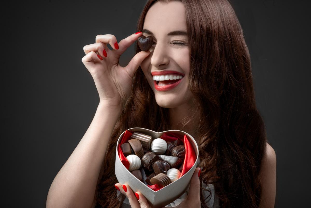 Best and Worst Valentine’s Day Candies Woman with bright smile holding heart-shaped chocolate box, illustrating Valentine's candy choices.