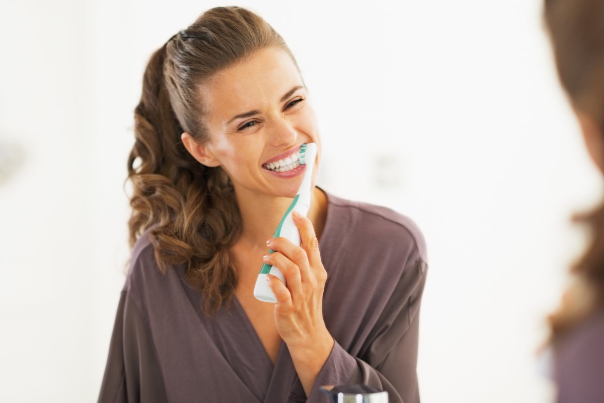 Woman brushing her teeth with an electric toothbrush and smiling.
