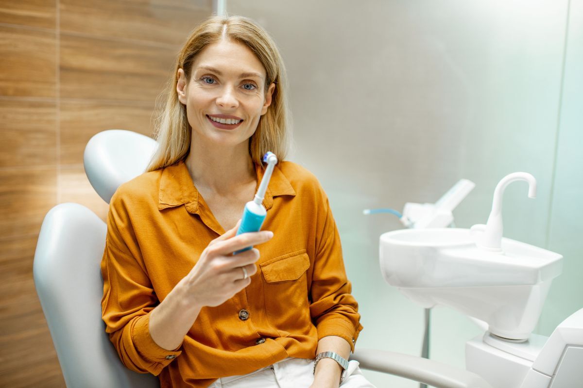 3 Features to Look for in an Electric Toothbrush Woman holding electric toothbrush in dental office treatment room.
