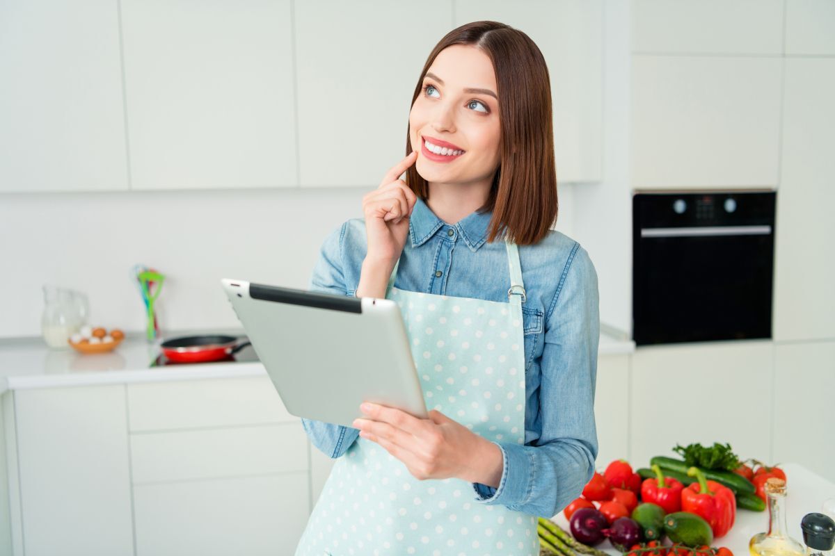 Woman in kitchen reviewing healthy lunch recipe on tablet with fresh vegetables for optimal dental health.
