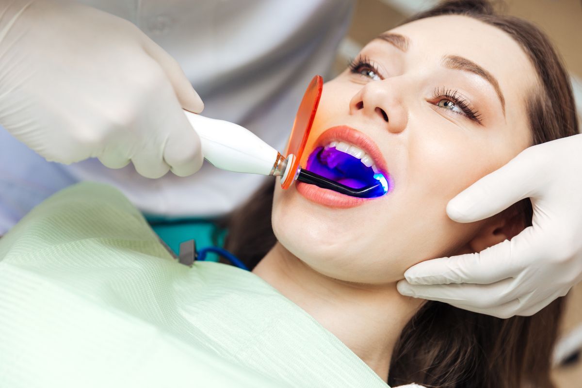 Dentist using UV light to whiten patient's teeth during professional whitening treatment.
