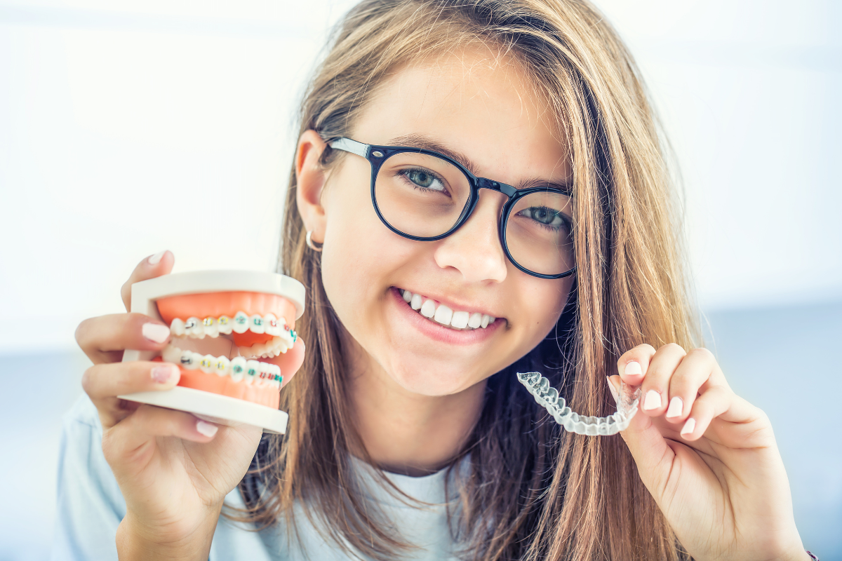 Young girl wearing glasses holding a dental model with braces and clear aligner tray.