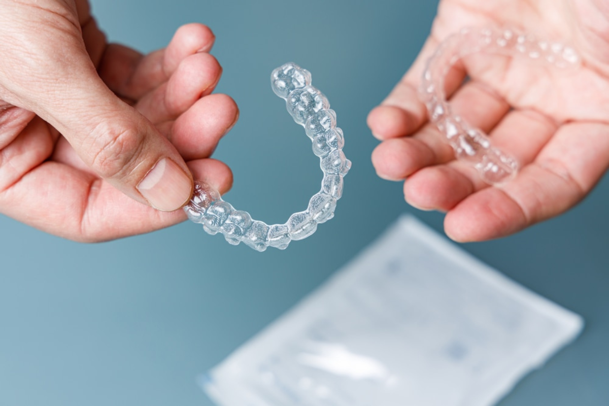 Hands holding a clear Invisalign aligner tray against a blue background.