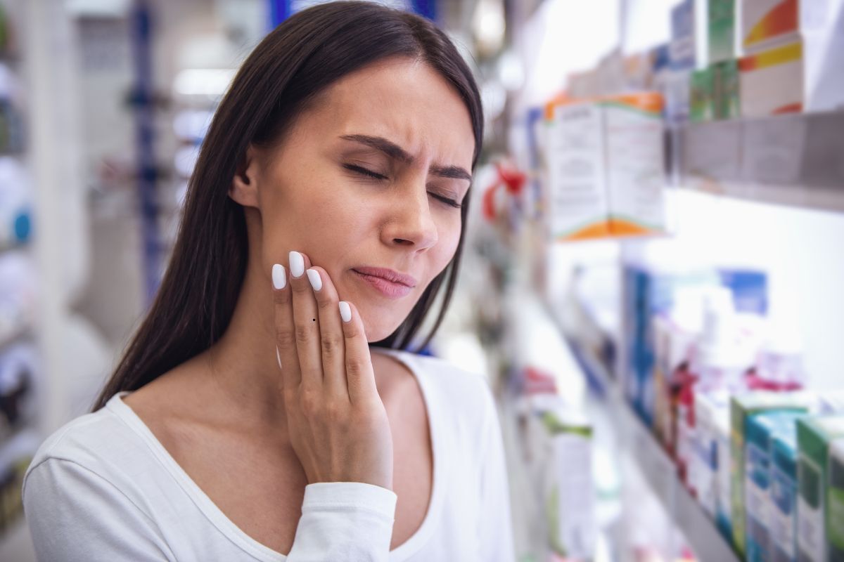 Lost Filling or Crown What to Do Before Seeing an Emergency Dentist Woman holding her cheek in pain at a pharmacy, experiencing dental discomfort.