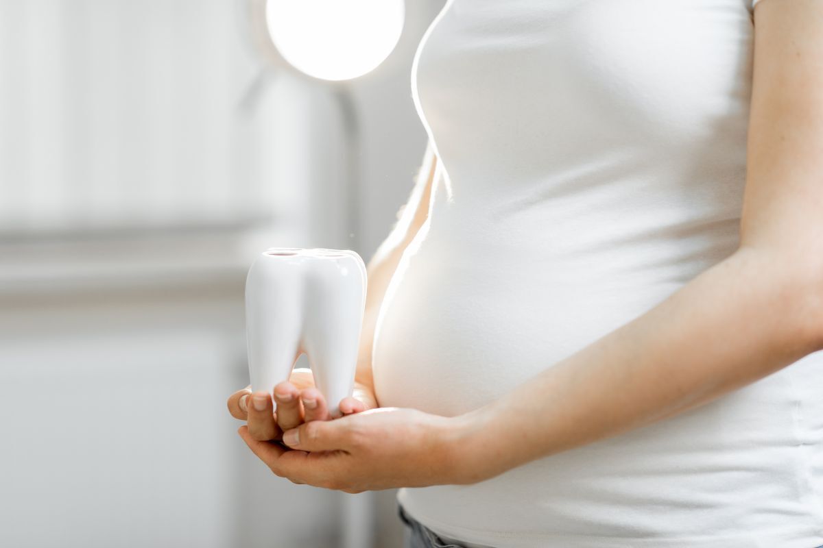 Pregnant woman holding a white tooth model, representing prenatal dental health care.