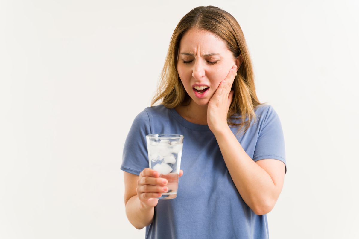 Woman with sensitive tooth pain holding a glass of ice water.
